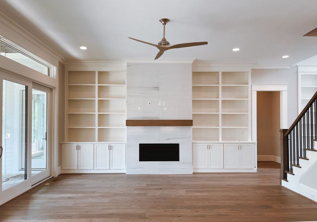 White built-in shelves and lower cabinets framing a fireplace in an empty living room