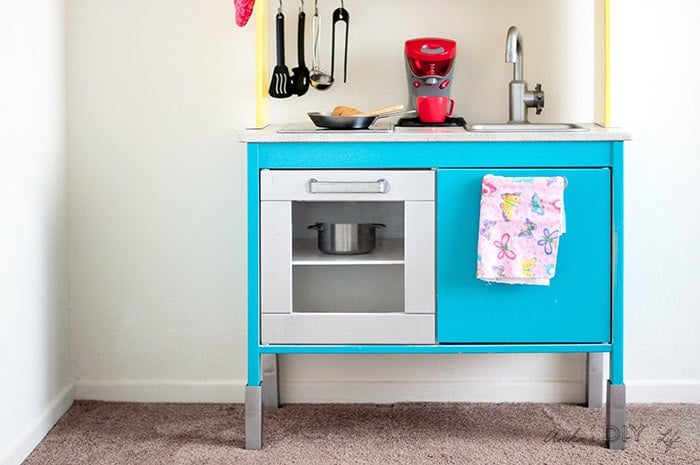 IKEA DUKTIG play kitchen with turquoise cabinets, a silver oven door and sink, and a floral hand towel